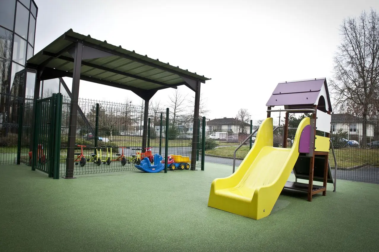 Cour extérieure sécurisée avec tricycles et porteurs à la crèche La Maison Kangourou Brive