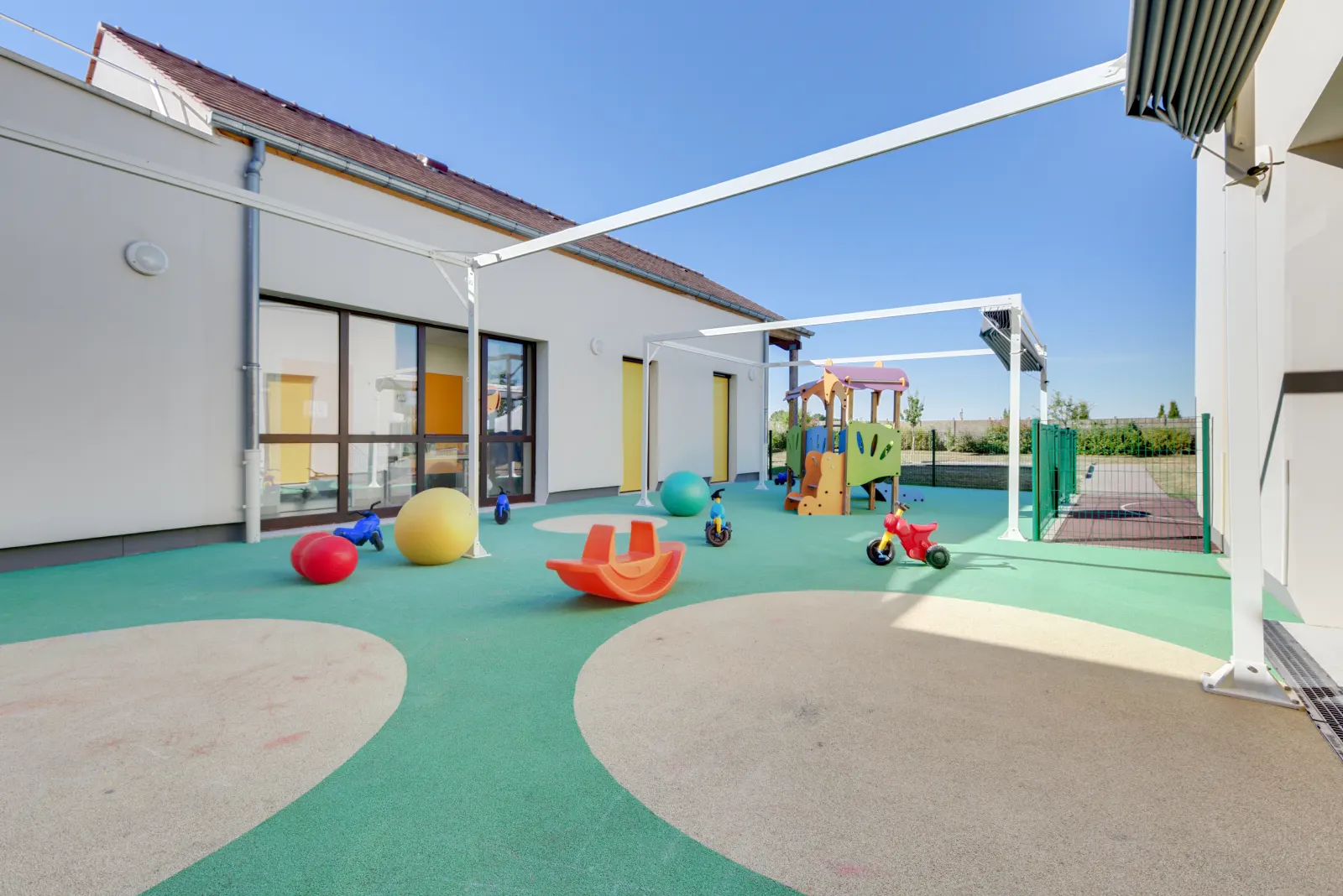 Cour extérieure avec tricycles et structure de jeux à la crèche Ennery Les Coquelicots