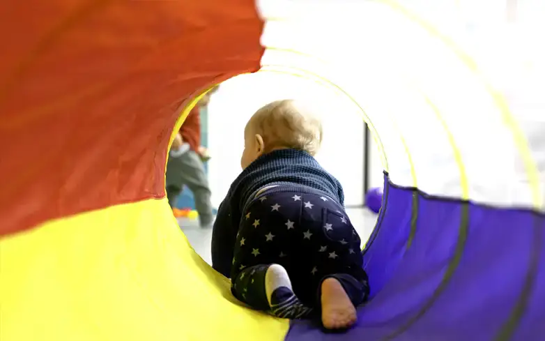 Enfant explorant un tunnel de motricité à la micro-crèche Les Dames